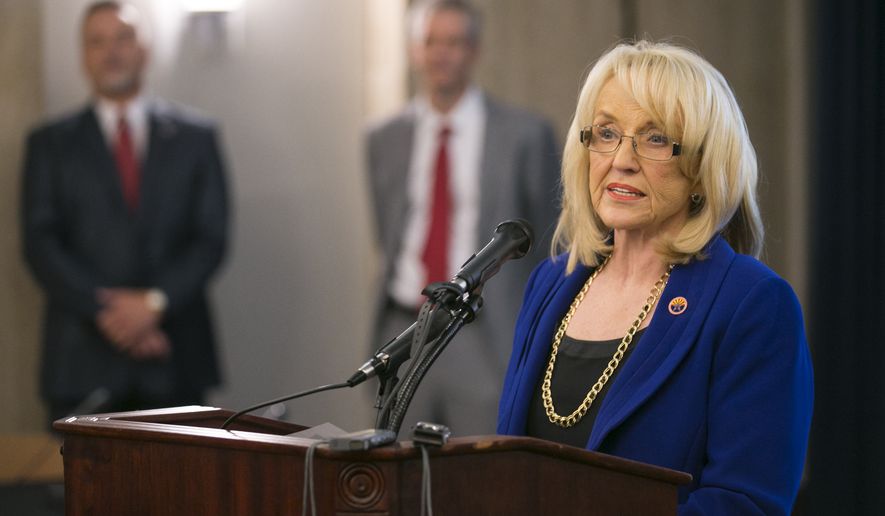 Gov. Jan Brewer speaks during a press briefing on the plan to create a new child-welfare agency in front of Charles Flanagan, (background left) director of the Division of Child Safety and Family Services and John Arnold, Gov. Brewer's Budget Director, in the executive tower at the Arizona state capitol in Phoenix on Thursday, May 22, 2014. (AP Photo/The Arizona Republic, David Wallace)