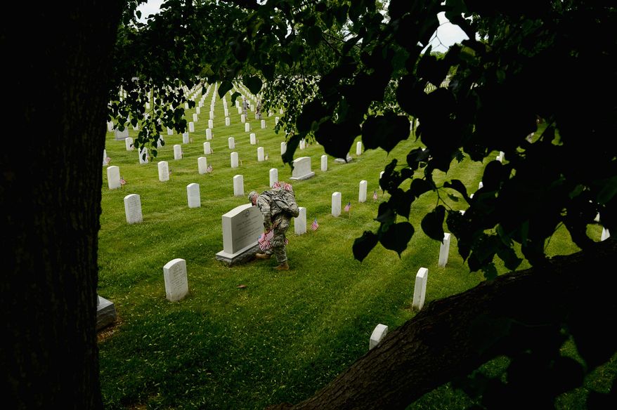 Army Private Tobias Tirrell with the Third U.S. Infantry Regiment (The Old Guard) places a small American flag at a grave marker to honor the nations fallen members of the military at Arlington National Cemetery, Washington, D.C, Thursday, May 22, 2014. The Old Guard placed flags for more than 220,000 graves. (Andrew Harnik/The Washington Times)
