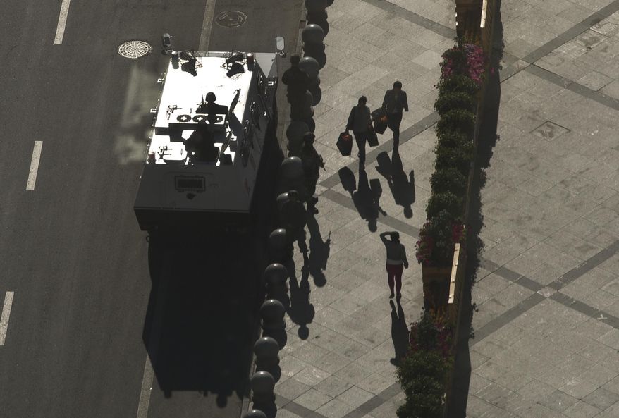 People walk past an armed paramilitary policemen stand guard next to their armored personnel carrier parked near the People's Square in Urumqi, China's northwestern region of Xinjiang, Saturday, May 24, 2013. Local authorities said police have identified five suspects - four people who died in the attack and another who was caught Thursday - the official Xinhua News Agency reported. It said all five had "long been influenced by the religious extremism." Chinese authorities have blamed most recent attacks on radical separatists from the country's Muslim Uighur minority. (AP Photo/Andy Wong)