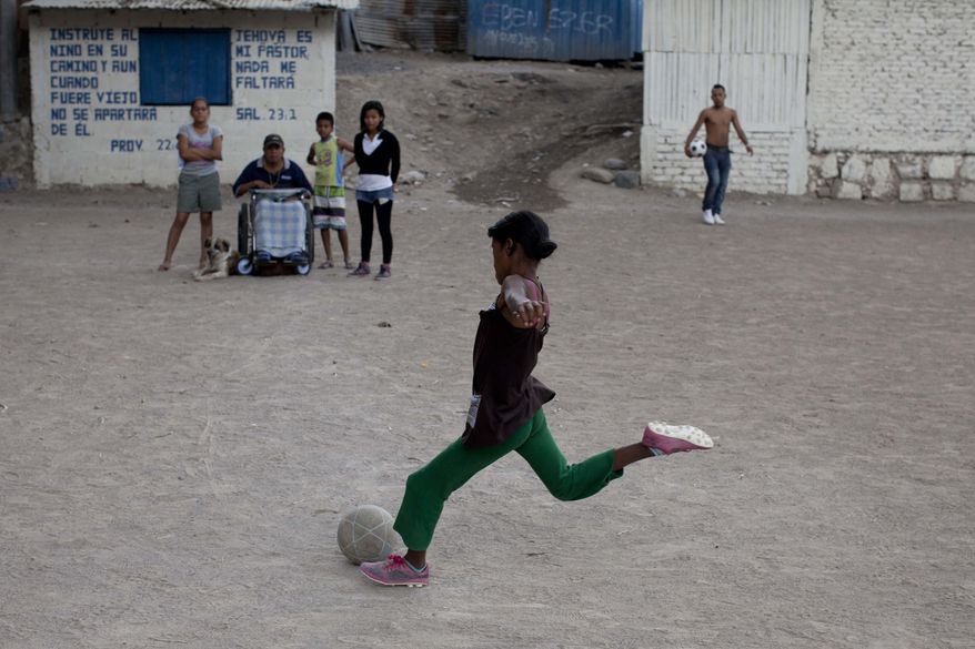 In this Wednesday, March 5, 2014 photo, a girl kicks the soccer ball as coach Luis Lopez watches from his wheelchair in the Progreso neighborhood of Tegucigalpa, Honduras. Luis, or Luisito as the trainer is affectionately called, is teaching these boys and girls to play soccer, knowing that the real game for them is to stay alive. Behind on the wall next to the field is a passage in Spanish from Proverbs, "Train up a child in the way he should go: and when he is old, he will not depart from it." (AP Photo/Dario Lopez-Mills)