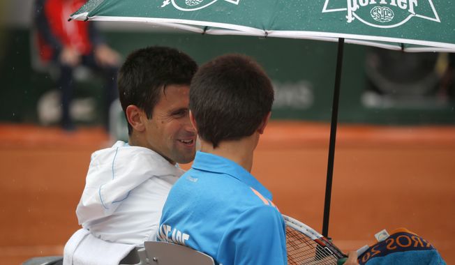 Serbia's Novak Djokovic, left, talks to a ball boy after inviting him to sit on his bench during a break during the first round match of the French Open tennis tournament against Portugal's Joao Sousa at the Roland Garros stadium, in Paris, France, Monday, May 26, 2014. (AP Photo/Michel Euler)