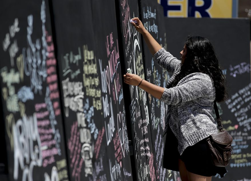 Daniela Bayon writes on a remembrance wall across the street from the IV Deli Mart, where part of the mass killings took place, on Tuesday, May 27, 2014 in the Isla Vista area near Goleta, Calif. Sheriff's officials said Elliot Rodger, 22, went on a rampage near the University of California, Santa Barbara, stabbing three people to death at his apartment before shooting and killing three more in a crime spree through a nearby neighborhood. (AP Photo/Chris Carlson)