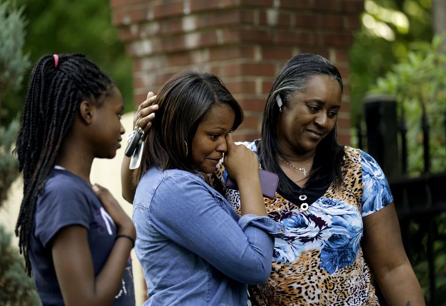 Dezmonee Selbey, center, is comforted by her mother Darretta Rhone, right, and sister Imani Rhone as they look over a memorial of flowers outside the home of Maya Angelou in Winston-Salem, N.C., Wednesday, May 28, 2014. Angelou has died at the age of 86. (AP Photo/Gerry Broome)