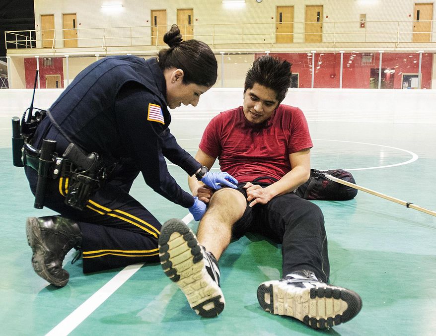 In this April 3, 2014 photo, Northern Illinois University police officer Maria Christiansen checks on NIU senior Juan Martinez during a floor hockey game on campus before calling paramedics to assist in DeKalb, Ill. Christiansen, a survivor of the Feb. 14, 2008 NIU school shooting that injured 21 and killed five students, works the night shift on campus patrol. (AP Photo/Daily Chronicle, Danielle Guerra) MANDATORY CREDIT