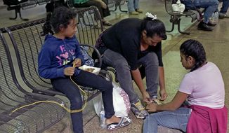 Elana Carmen, middle, with her daughters Abigail, right, and Ayala, of El Salvador, tie their shoes with yellow rope for shoe laces, Thursday, May 29, 2014 at the Greyhound bus terminal in Phoenix. About 400 mostly Central American women and children caught crossing from Mexico into south Texas were flown to Arizona this weekend after border agents there ran out of space and resources.  Officials then dropped hundreds of them off at Phoenix and Tucson Greyhound stations, overwhelming the stations and humanitarian groups who were trying to help. (AP Photo/Rick Scuteri)