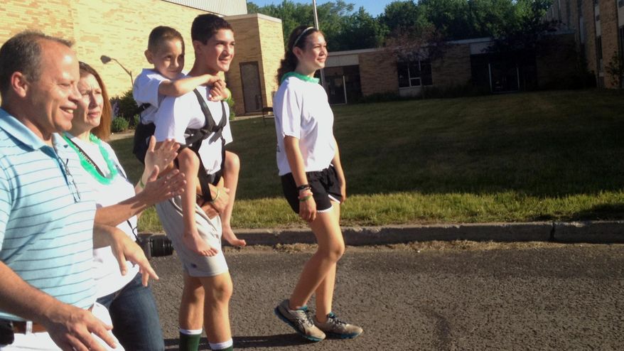 Hunter Gandee, 14, holds his brother Braden Gandee, 7, in a harness on his back on Saturday, June 7, 2014, in Temperance, Mich. Hunter set out on a 40-mile trek on Saturday with his brother hoping to raise awareness about the muscular condition, Cerebral Palsy Swagger, that prevents the younger boy from being able to walk without help. (AP Photo/Detroit Free Press, Eric D. Lawrence) DETROIT NEWS OUT; NO SALES