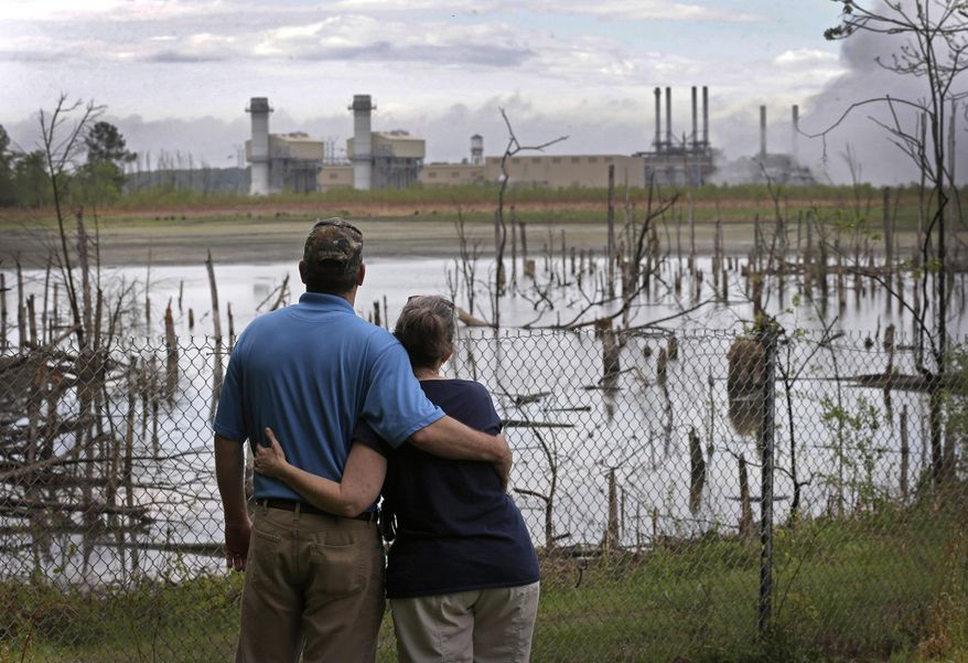 In this April 25, 2014, photo, Bryant Gobble, left, hugs his wife, Sherry Gobble, right, as they look from their yard across an ash pond full of dead trees toward Duke Energy's Buck Steam Station in Dukeville, N.C. (AP Photo/Chuck Burton)