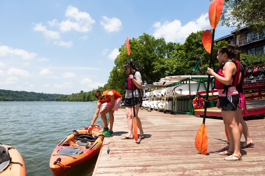 Jami Harp, from Fort Worth Texas, gets ready to sit in her kayak as deckstaff Connor Ryan of Key Bridge Boathouse rentals helps her get settled Tuesday afternoon. The days warm weather would bring out a steady stream of visitors to the river. Keith Lane/Special to the Washington Times