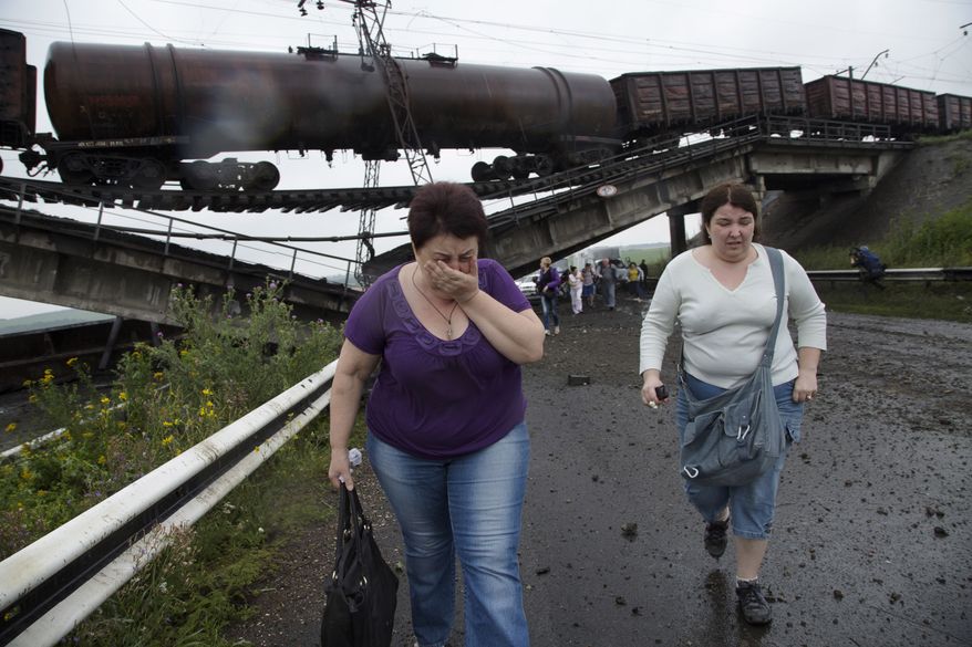 People walk under a destroyed railroad bridge over a main road leading into the east Ukraine city of Donetsk, near the village of Novobakhmutivka, 20 km North from the city of Donetsk, eastern Ukraine Monday, July 7, 2014. The bridge has been destroyed, blocking a key access route to the rebel-held city. (AP Photo/Dmitry Lovetsky)
