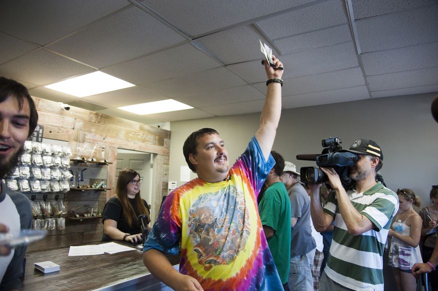 ** FILE ** Mike Boyer turns to the crowd outside, showing off the 4 grams of marijuana he bought as the first in line to legally purchase marijuana at Spokane Green Leaf, Tuesday, July 8, 2014, in Spokane, Wash. (Associated Press)