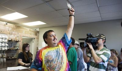 Mike Boyer turns to the crowd outside, showing off the 4 grams of marijuana he bought as the first in line to legally purchase marijuana at Spokane Green Leaf, Tuesday, July 8, 2014, in Spokane, Wash.  (AP Photo/The Spokesman-Review, Dan Pelle)