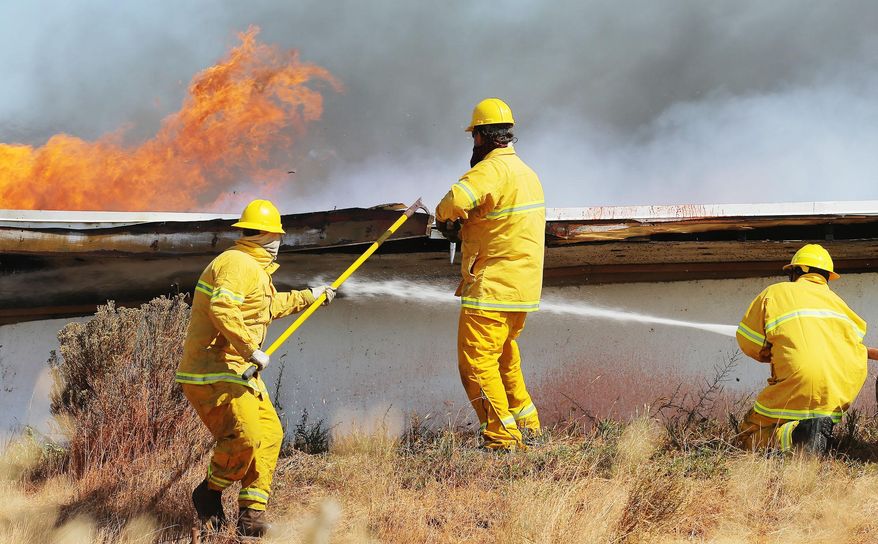 Firefighters from Stockton and Tooele Utah work Wednesday, July 16, 2014, to put out flames burning on the city's water tank. Officials say a wildfire encroaching on homes in the Tooele County town of Stockton has overtaken 400-500 acres. Utah Division of Forestry, Fire and State Lands spokesman Jason Curry says he believes no homes have been destroyed. (AP Photo/The Deseret News, Scott G Winterton)