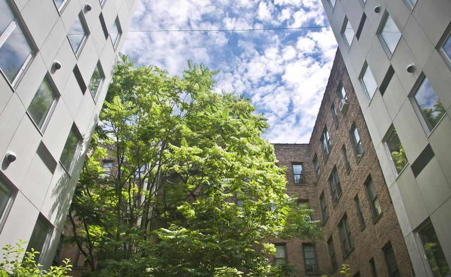 A patio garden view shows a seven-story modern modular apartment building called the Stack, on either side of a decades-old residence, Wednesday, July 9, 2014, in the Innwood neighborhood of New York. The Stack's 28 apartments were formed from 59 modules of rectangular components all 12.5 feet wide and 50 to 60 feet long. It’s billed as the first multistory, modular-built apartment building to open in the city. (AP Photo/Bebeto Matthews)