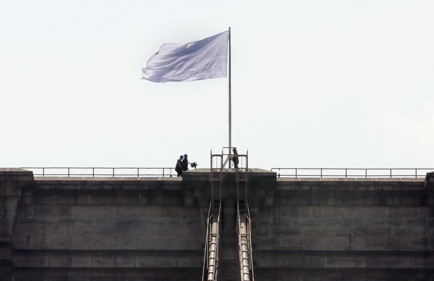 New York City Police officers stand at the base of a white flag flying atop the west tower of New York's Brooklyn Bridge, Tuesday, July 22, 2014. Two large American flags atop the Brooklyn Bridge were replaced sometime during the night with white banners. Police crime scene and intelligence detectives were investigating how the flags were switched out on the famed span that connects Brooklyn and Manhattan, and there were no reports of suspicious activity, police said. (AP Photo/Richard Drew)