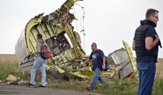 Malaysian air crash investigators walk by wreckage at the crash site of Malaysia Airlines Flight 17 near the village of Hrabove, eastern Ukraine, Tuesday, July 22, 2014. A team of Malaysian investigators visited the site along with members of the OSCE mission in Ukraine for the first time since the air crash last week.(AP Photo/Vadim Ghirda)