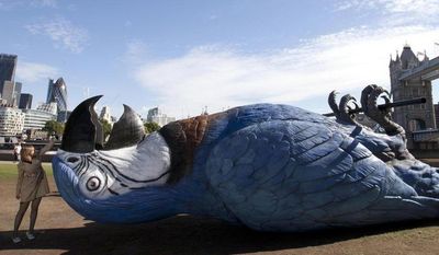 In this photo taken Monday, July 14, 2014, a person stands alongside a sculpture depicting a giant dead parrot measuring 15 meters (49 feet) as it is unveiled to promote what is being billed as the final Monty Python live stage show which will be broadcast on Sunday, July 20, near Tower Bridge, London. (AP Photo/PA, David Parry) UNITED KINGDOM OUT, NO SALES, NO ARCHIVE
