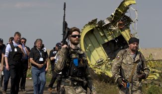 A pro-Russian rebel holds a gun passing by plane wreckage as members of the OSCE mission to Ukraine arrive for a media briefing at the crash site of Malaysia Airlines Flight 17, near the village of Hrabove, eastern Ukraine, Tuesday, July 22, 2014. (AP Photo/Vadim Ghirda) ** FIL E**