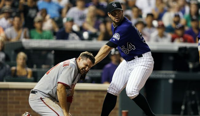 Colorado Rockies relief pitcher Tommy Kahnle (54) applies a late tag to the face of Washington Nationals&#x27; Ryan Zimmerman (11)  during the seventh inning of a baseball game on Monday, July 21, 2014, in Denver. Zimmerman scored on the play. (AP Photo/Jack Dempsey)