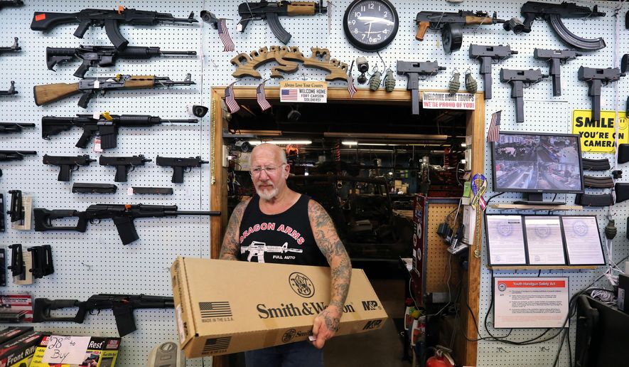 In this July 20, 2014 photo, gun dealer Mel Bernstein carries box for a rifle while making a sale at his store, Dragonman&#39;s, east of Colorado Springs, Colo. When Colorado lawmakers expanded background checks on firearms last year, they were expecting a huge increase. But the actual number the first 12 months of the law is far lower than projected, according to an analysis of state data by The Associated Press. (AP Photo/Brennan Linsley)