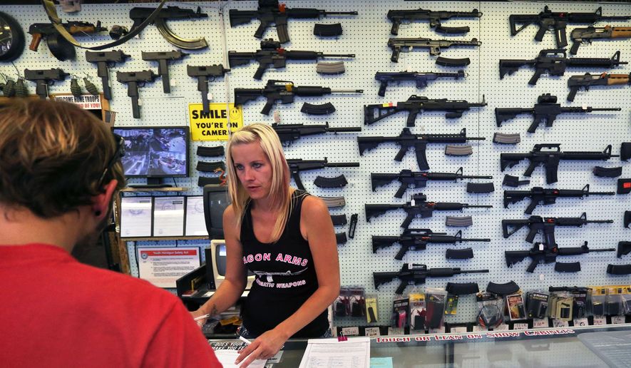 ** FILE ** In this July 20, 2014, photo, with guns displayed for sale behind her, a gun store employee helps a customer at Dragonman&#39;s, east of Colorado Springs, Colo. (AP Photo/Brennan Linsley)