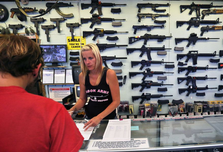 ** FILE ** In this July 20, 2014, photo, with guns displayed for sale behind her, a gun store employee helps a customer at Dragonman's, east of Colorado Springs, Colo. (AP Photo/Brennan Linsley)