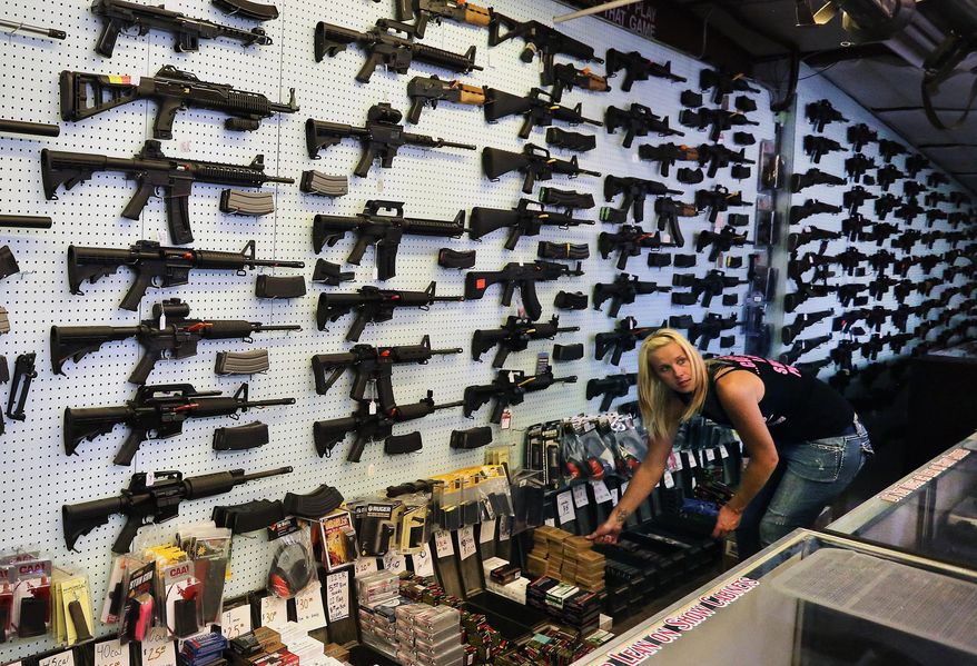 In this July 20, 2014 photo, with guns displayed for sale behind her, a gun store employee helps a customer at Dragonman's, east of Colorado Springs, Colo. When Colorado lawmakers expanded background checks on firearms last year, they were expecting a huge increase. But the actual number the first 12 months of the law is far lower than projected, according to an analysis of state data by The Associated Press. (AP Photo/Brennan Linsley)