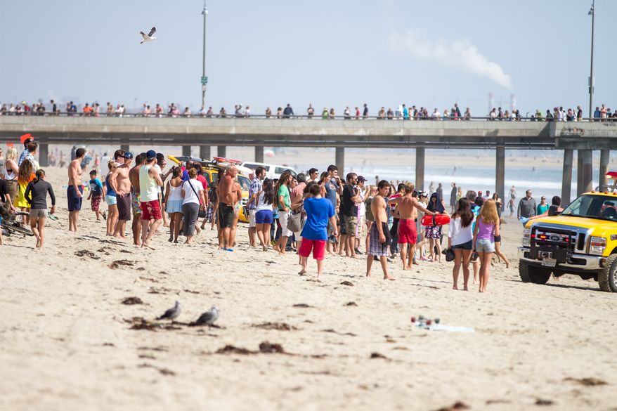 Pedestrians and beachgoers stand on the shore near Venice Beach as lifeguards, right, bring in a swimmer rescued from the water after a lightening strike Sunday, July 27, 2014, in Los Angeles. (AP Photo/Steve Christenesn)