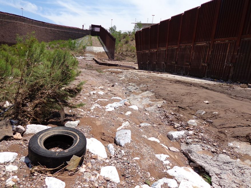 A section of fence lies collapsed just west of the Mariposa Port of Entry in Nogales, Ariz., Sunday, July 27, 2014, after severe storms in southern Arizona over the weekend knocked down a chunk of the metal border fence that divides Mexico and the U.S. Rain runoff from the storms destroyed about 60 feet worth of fence and caused damage to homes just north of it. (AP Photo/Nogales International, Jonathan Clark)