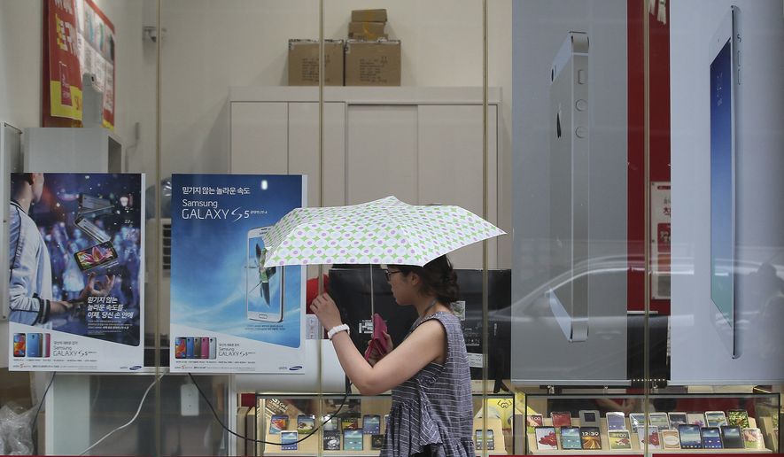 A woman walks by advertisement posters of Samsung Electronics&#39; Galaxy S5, Apple&#39;s iPhone 5s and iPad Air at a mobile phone shop in Seoul, South Korea, Wednesday, Aug. 6, 2014. Samsung and Apple Inc. have agreed to end all patent lawsuits between each other outside the U.S. in a step back from three years of legal hostilities between the world&#39;s two largest smartphone makers. (AP Photo/Ahn Young-joon)