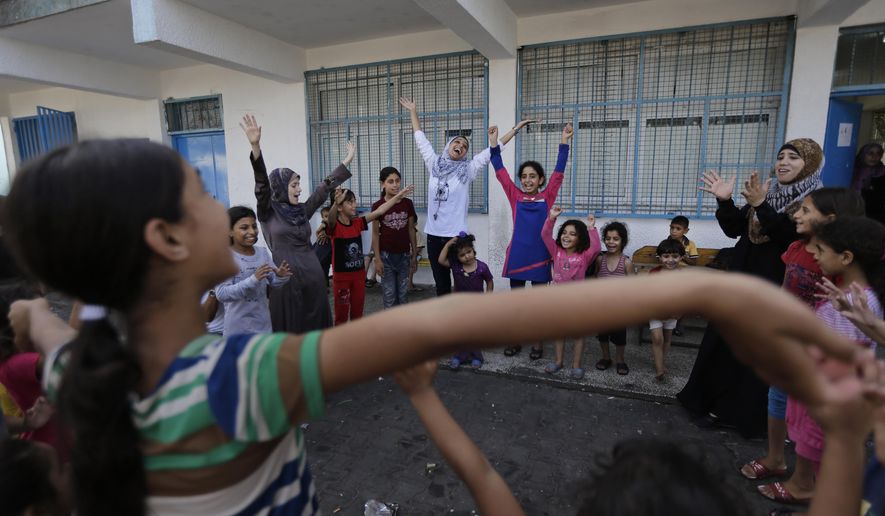Volunteer Nisreen Shawa, 25, centre, leads a play session with displaced Palestinian children at a U.N. school where they had sought refuge along with their families during the war, in Gaza City, Gaza Strip, Thursday, Aug. 7, 2014. Taking advantage of the continuing ceasefire, volunteers from the local non-profit NGO 'Tomooh' (Ambition), arranged a special play session for children to try and lessen the stress they've been enduring after the weeks of conflict. In the playground the children got a chance to sing and play group games under the caring eye of volunteers. They hope that their efforts will lessen the damage of the traumatic recent weeks events, or at least help them forget for a short while. (AP Photo/Lefteris Pitarakis)