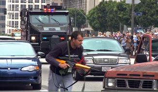 In this July 6, 2013 still frame from a video produced by the Los Angeles Police Department, a man posing as a terrorist runs as a heavily-armored vehicle approaches in a drill simulating a terrorist attack in downtown Los Angeles. After spending a decade sending military equipment to civilian police departments across the United States, Washington is reconsidering the idea in light of the violence in Ferguson, Mo., amid images of heavily-armed police, snipers trained on protesters and tear gas plumes. One night after the violence that accompanied the presence of military-style equipment in Ferguson, the crowd calmed considerably when a police captain walked through the crowd, unprotected, in a gesture of reconciliation. The contrast added to the perception that the tanks and tear gas had done more harm than good. (AP Photo/Los Angeles Police Department)