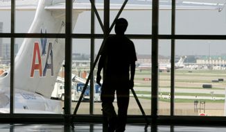 **FILE** The tail of an American Airlines aircraft is seen at left as a person walks by a passenger gate area in Terminal C at Dallas-Fort Worth International Airport in Grapevine, Texas, on Aug. 26, 2008. (Associated Press)