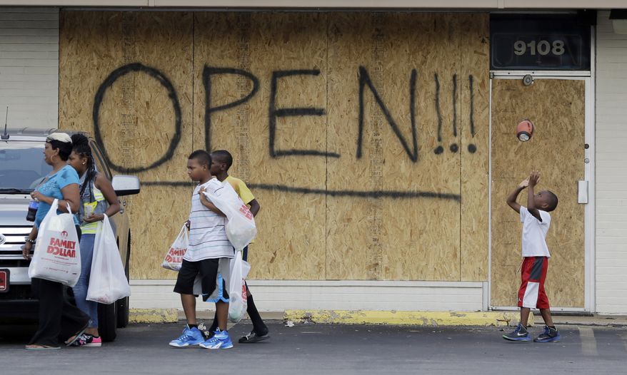 A young boy tosses a football as people walk past a business boarded up to protect against looting Monday, Aug. 18, 2014, in Ferguson, Mo. Missouri Gov. Jay Nixon called in the National Guard Monday after police again used tear gas to quell protesters in the wake of the shooting of Michael Brown. (AP Photo/Jeff Roberson)