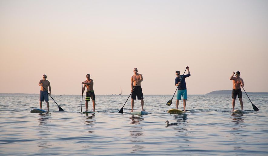 In a photo provided by John A. Gessner, stand-up paddle boarders from left, Jeff Guy, Kwin Morris, Joel Mueller, Andrew Pritchard, and Joe Lorenz all of Traverse City, Mich. are seen on a West Grand Traverse Bay beach. The five friends who all have a passion for watersports and the preservation of the Great Lakes plan to paddle across Lake Michigan to raise money for the Alliance for the Great Lakes. The 60 mile journey, referred to as Stand Up for Great Lakes, begins at Algoma, Wisconsin, and ends at Frankfort, Michigan, according to the Petoskey News-Review. (AP Photo/John A. Gessner Photography)