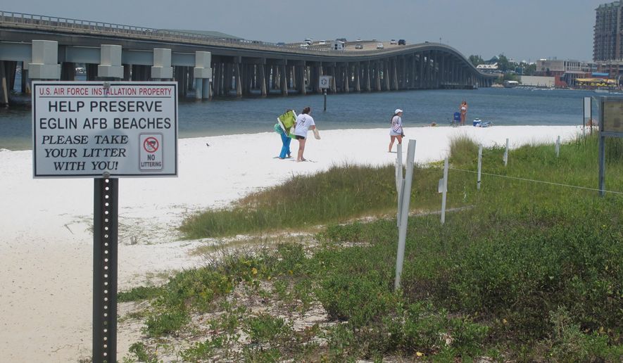In this July 7, 2014 photo, people look for a place to set up on a shallow beach under a highway bridge in Destin, Fla. The beach is under the controlled of Eglin Air Force Base where it is occasionally used to practice amphibious landings and test high-tech weapons. The public is welcome to use the beach. (AP Photo/Melissa Nelson-Gabriel)