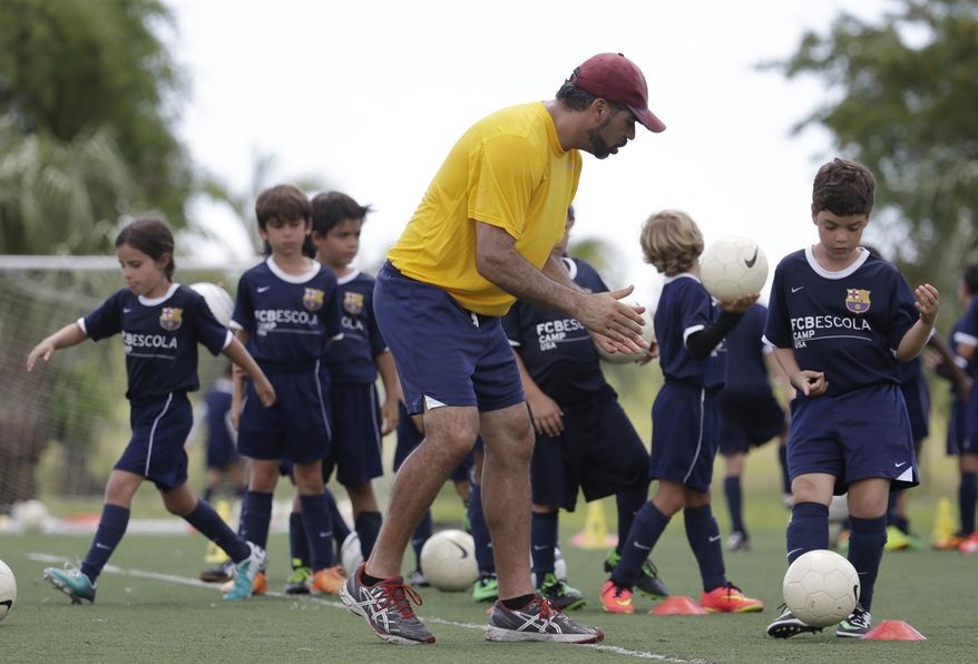 In this Thursday, Aug. 1, 2014 photo, Lee Santamaria, front, of Cooper City, Fla., works with children during a soccer camp held by FC Barcelona in Miami. European clubs like Barcelona, Liverpool and Arsenal have long sent coaches to work at U.S. summer camps, but now some are opening year-round U.S. academies aimed at finding new talent but also to expand their fan bases. This is part of a number of initiatives of major teams to grow their brands in the U.S. (AP Photo/Lynne Sladky)