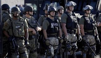 ** FILE ** Police watch protesters in Ferguson, Mo. on Wednesday, Aug. 13, 2014. (Associated Press)