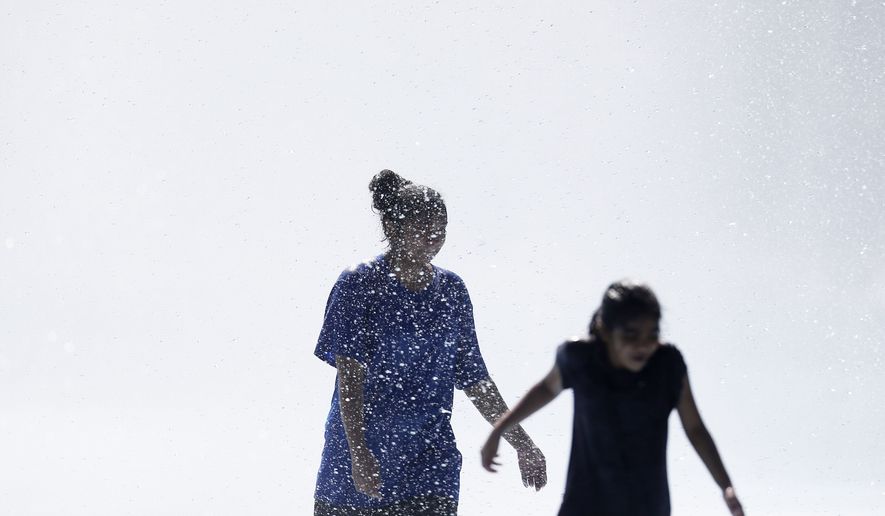 Young women play in the fountains surrounding the Unisphere at Flushing Meadows Corona Park in New York Sunday, Aug. 24, 2014. (AP Photo/Matt Rourke)