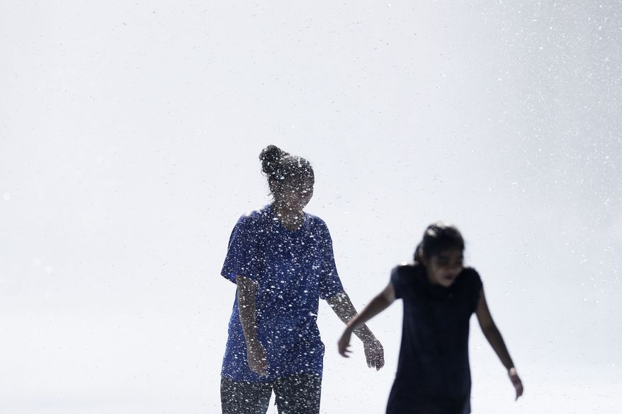 Young women play in the fountains surrounding the Unisphere at Flushing Meadows Corona Park in New York Sunday, Aug. 24, 2014. (AP Photo/Matt Rourke)