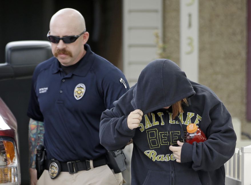 A unidentified woman is escorted from a home by a police officer after a baby was found in a garbage can in Kearns, Utah on Tuesday, Aug. 26, 2014. Police say the newborn is in extremely critical condition he was left in a trash can near his mother's home. Unified Police Detective Jared Richardson says a woman who lived nearby heard what she thought was a kitten meowing in the trash bin on Tuesday morning. (AP Photo/Rick Bowmer)