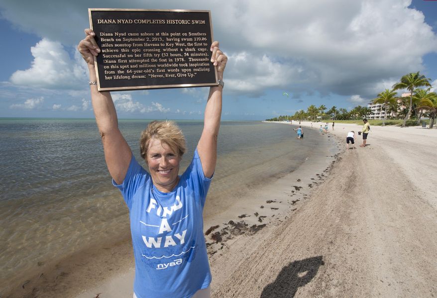 In this photo provided by the Florida Keys News Bureau, Diana Nyad poses with a bronze plaque Monday, Sept. 1, 2014, at Smathers Beach in Key West, Fla. The plaque commemorates Nyad's 2013 Cuba-to-Florida Keys swim. She arrived at Smathers Beach the early afternoon of Sept. 2, 2013, to become the first person to ever swim from Havana to Key West without a shark cage. (AP Photo/Florida Keys News Bureau, Andy Newman)