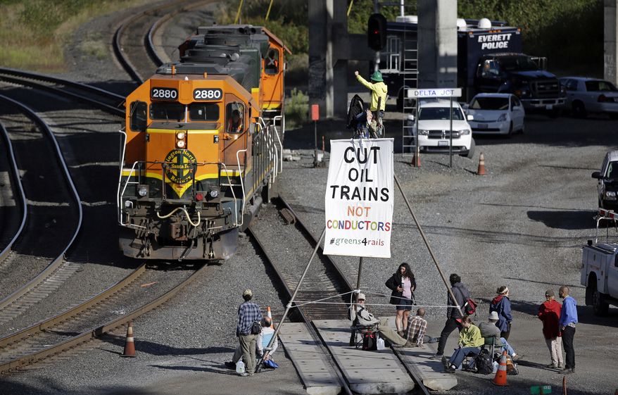 Abby Brockway waves from atop a tripod erected on train tracks to a pair of engines passing on an adjacent track Tuesday, Sept. 2, 2014, in Everett, Wash. About a dozen demonstrators blocked the tracks at a Burlington Northern Santa Fe yard to protest oil and coal export terminals in the Northwest. (AP Photo/Elaine Thompson)