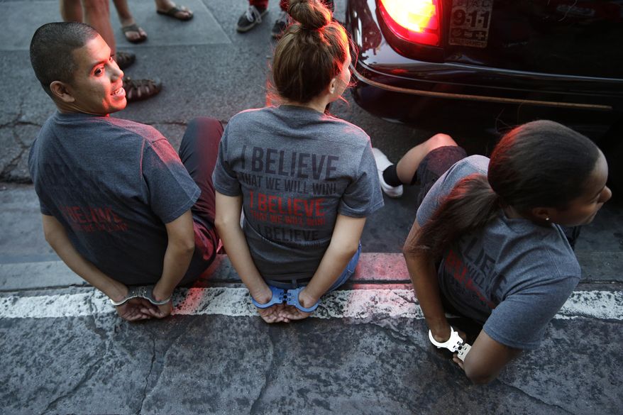 Handcuffed protestors sit on a curb Thursday, Sept. 4, 2014, in Las Vegas. Police detained several protesters in cities nationwide Thursday as they blocked traffic in the latest attempt to escalate their efforts to get McDonald's, Burger King and other fast-food companies to pay their employees at least $15 an hour. (AP Photo/John Locher)