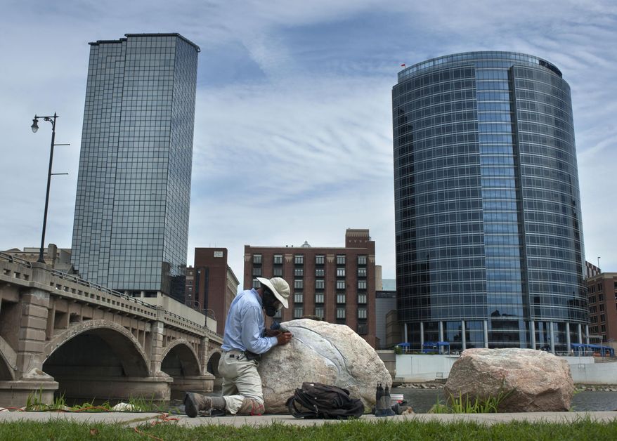 In this photo taken on Sept.4, 2014, artist Kevin Sudeith works on his ArtPrize entry titled "Grand River Fish Petroglyph" near the Grand Rapids Public Museum in Grand Rapids, Mich. Sudeith is carving images of the fish that navigate the river on rocks he has placed there. (AP Photo/The Grand Rapids Press, Chris Clark) ALL LOCAL TELEVISION OUT; LOCAL TELEVISION INTERNET OUT