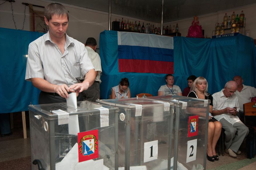 A man casts his ballot papers at a polling station set up in a cafe hall, with a Russian flag in the background, during regional parliament and municipal election in Sevastopol, Crimea, Sunday, Sept. 14, 2014. (AP Photo/Alexander Polegenko)