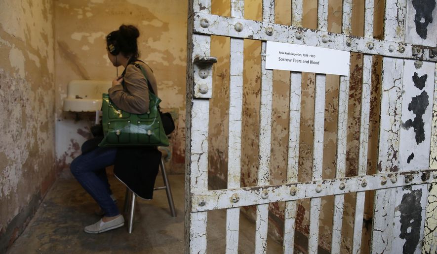 A woman sits in a cell and listens to a recording of Nigerian Fela Kuti that is part of the installation called Stay Tuned during a preview of the art exhibit @Large: Ai Weiwei on Alcatraz Island Wednesday, Sept. 24, 2014, in San Francisco. Revealing unexpected perspectives on Alcatraz and its layered legacy, the exhibit by the Beijing-based artist prompts visitors to consider the implications of incarceration and the possibilities of art as an act of conscience. The exhibit opens Friday and runs through April. Stay Tuned invites visitors into 12 individual cells in A Block, where they can sit and listen to spoken words, poetry and music by people who have been imprisoned for the creative expression of their beliefs. (AP Photo/Eric Risberg)