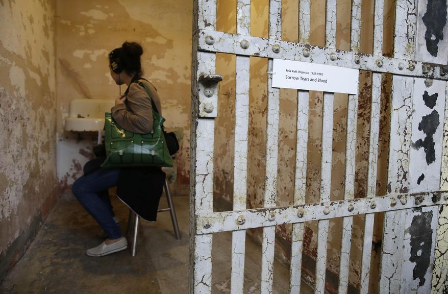 A woman sits in a cell and listens to a recording of Nigerian Fela Kuti that is part of the installation called Stay Tuned during a preview of the art exhibit @Large: Ai Weiwei on Alcatraz Island Wednesday, Sept. 24, 2014, in San Francisco. Revealing unexpected perspectives on Alcatraz and its layered legacy, the exhibit by the Beijing-based artist prompts visitors to consider the implications of incarceration and the possibilities of art as an act of conscience. The exhibit opens Friday and runs through April. Stay Tuned invites visitors into 12 individual cells in A Block, where they can sit and listen to spoken words, poetry and music by people who have been imprisoned for the creative expression of their beliefs. (AP Photo/Eric Risberg)