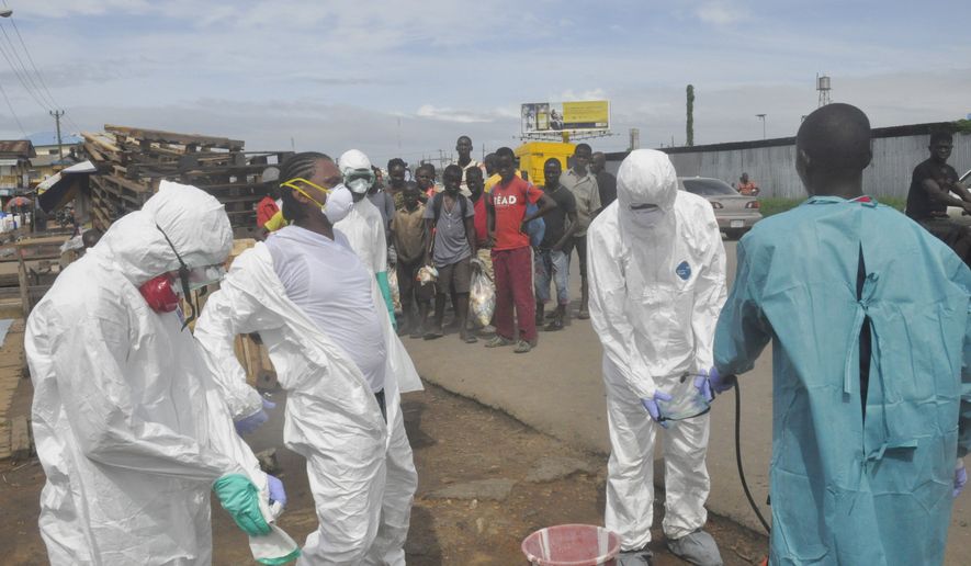 Onlookers watch as health workers in protective gear sprayed each other with disinfectant after they removed the body of a woman suspected of dying from Ebola virus, near the area of Freeport in Monrovia, Liberia, Wednesday, Oct. 1, 2014. The first case of Ebola diagnosed in the U.S. has been confirmed in a man who recently traveled from Liberia to Dallas. (AP Photo/Abbas Dulleh)