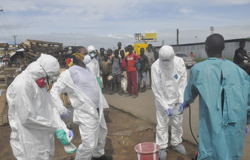 Onlookers watch as health workers in protective gear sprayed each other with disinfectant after they removed the body of a woman suspected of dying from Ebola virus, near the area of Freeport in Monrovia, Liberia, Wednesday, Oct. 1, 2014. The first case of Ebola diagnosed in the U.S. has been confirmed in a man who recently traveled from Liberia to Dallas. (AP Photo/Abbas Dulleh)