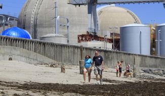 This June 30, 2011, file photo shows beach-goers walking on the sand near the San Onofre nuclear power plant in San Clemente, Calif. (AP Photo/Lenny Ignelzi, File)
